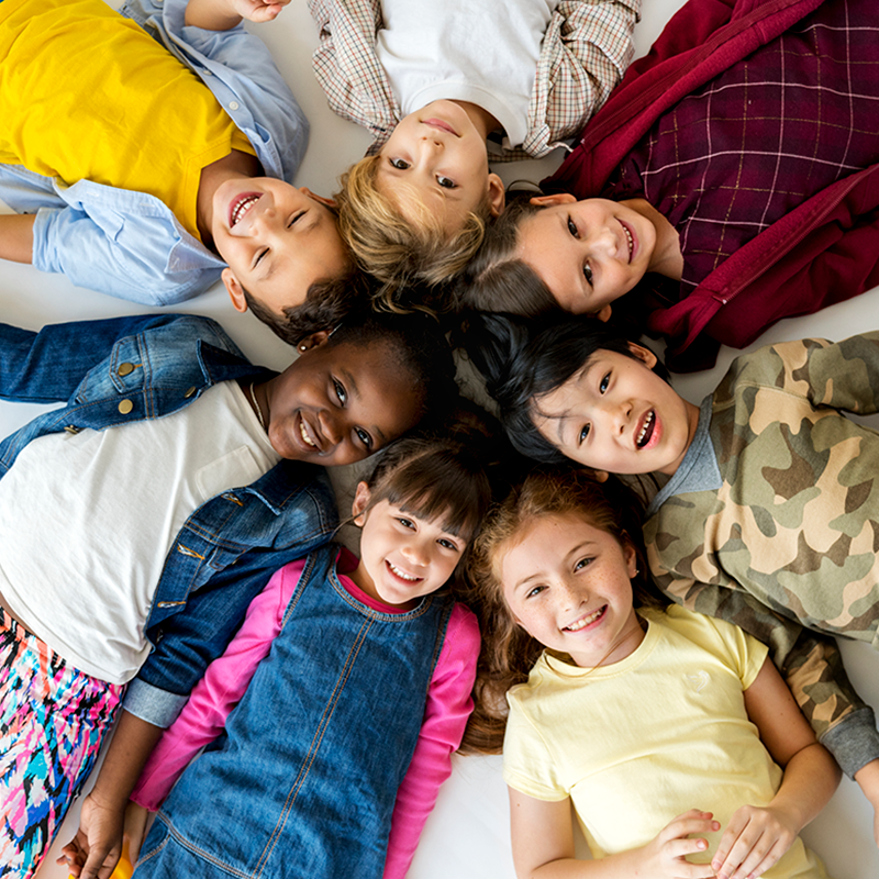 Group of diverse children laying on their backs staring up at the camera