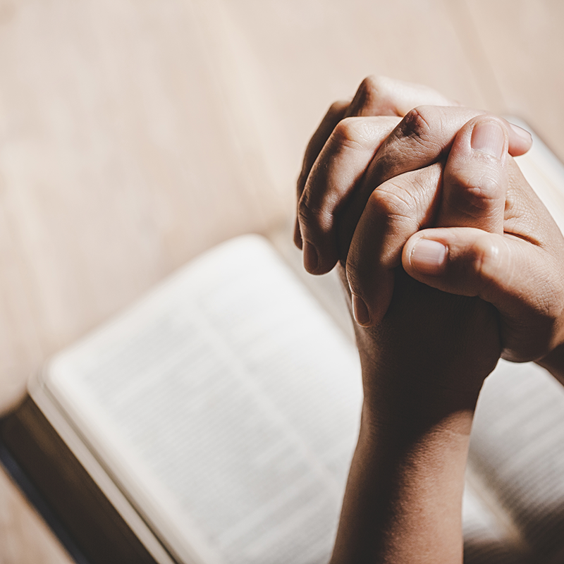 Clasped hands praying over an open Bible